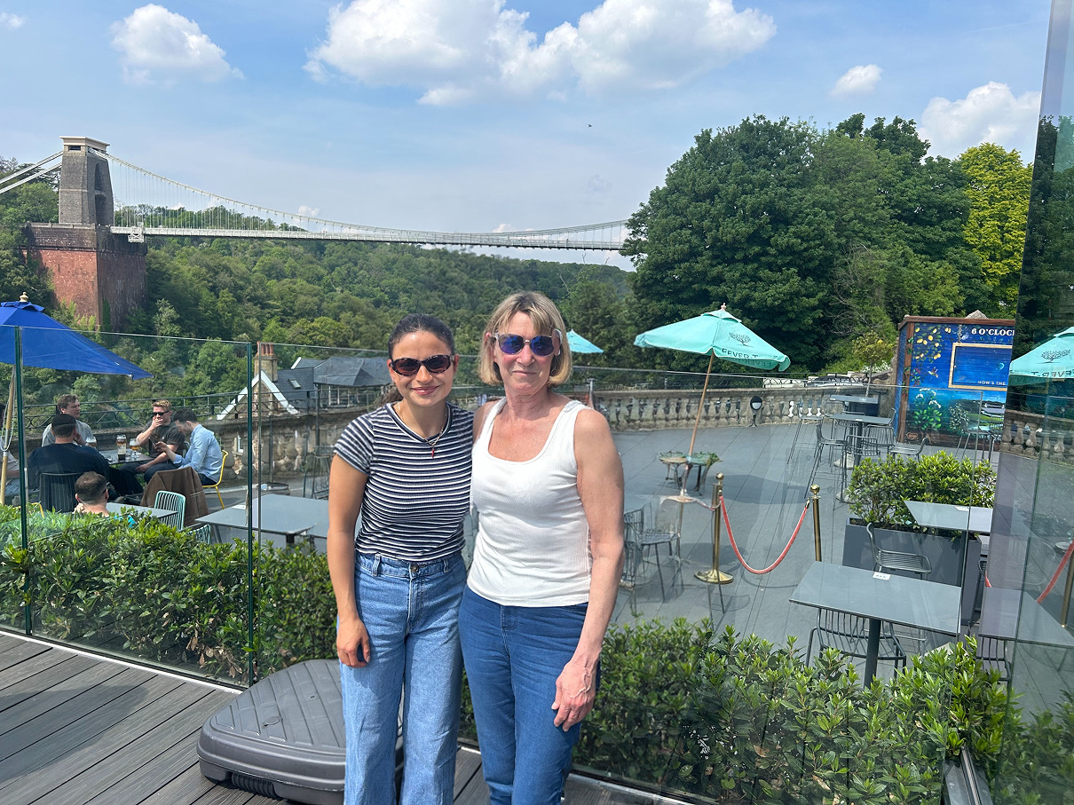 The same photo with the middle person removed and the remaining two people moved together, standing side by side with a naturally rebuilt background.